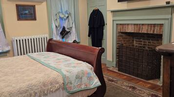 A bedroom with a bed, a ceiling fan, a fireplace, a TV, and a radiator.