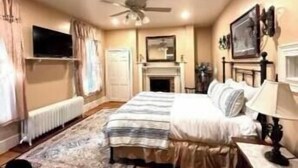 A bedroom with a bed, a fireplace, a ceiling fan, and a TV mounted on the wall. - Langdon Hill House (Gettysburg)
