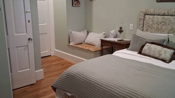A bedroom with a bed, bedside table, lamp, wall-mounted picture, and a door.