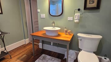 A bathroom with a wooden vanity, a white sink, a mirror with lights, a toilet, and a framed picture on the wall.