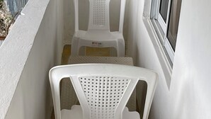 Un balcon étroit aux murs blancs, avec une fenêtre et deux chaises en plastique blanches.