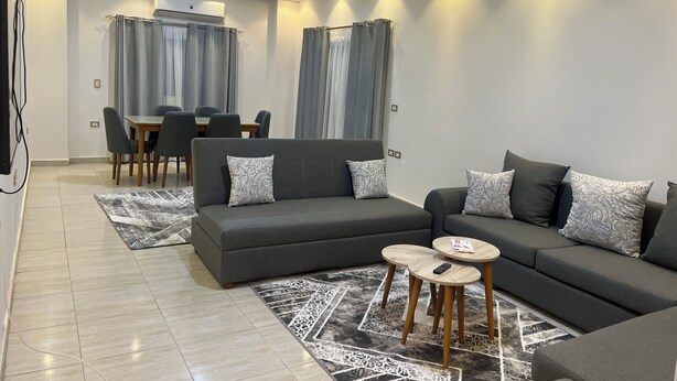 Ein modernes Wohnzimmer mit einem Ecksofa, einem Esstisch mit Stühlen und einem gemusterten Teppich.