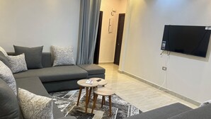 Ein modernes Wohnzimmer mit einer Eckcouch, einem Flachbildfernseher an der Wand und einem kleinen Holztisch.