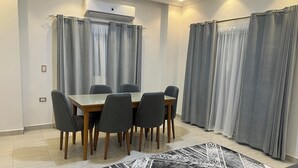 Ein Essbereich mit Tisch und Stühlen, grauen Vorhängen, einer Klimaanlage und einem gemusterten Teppich.