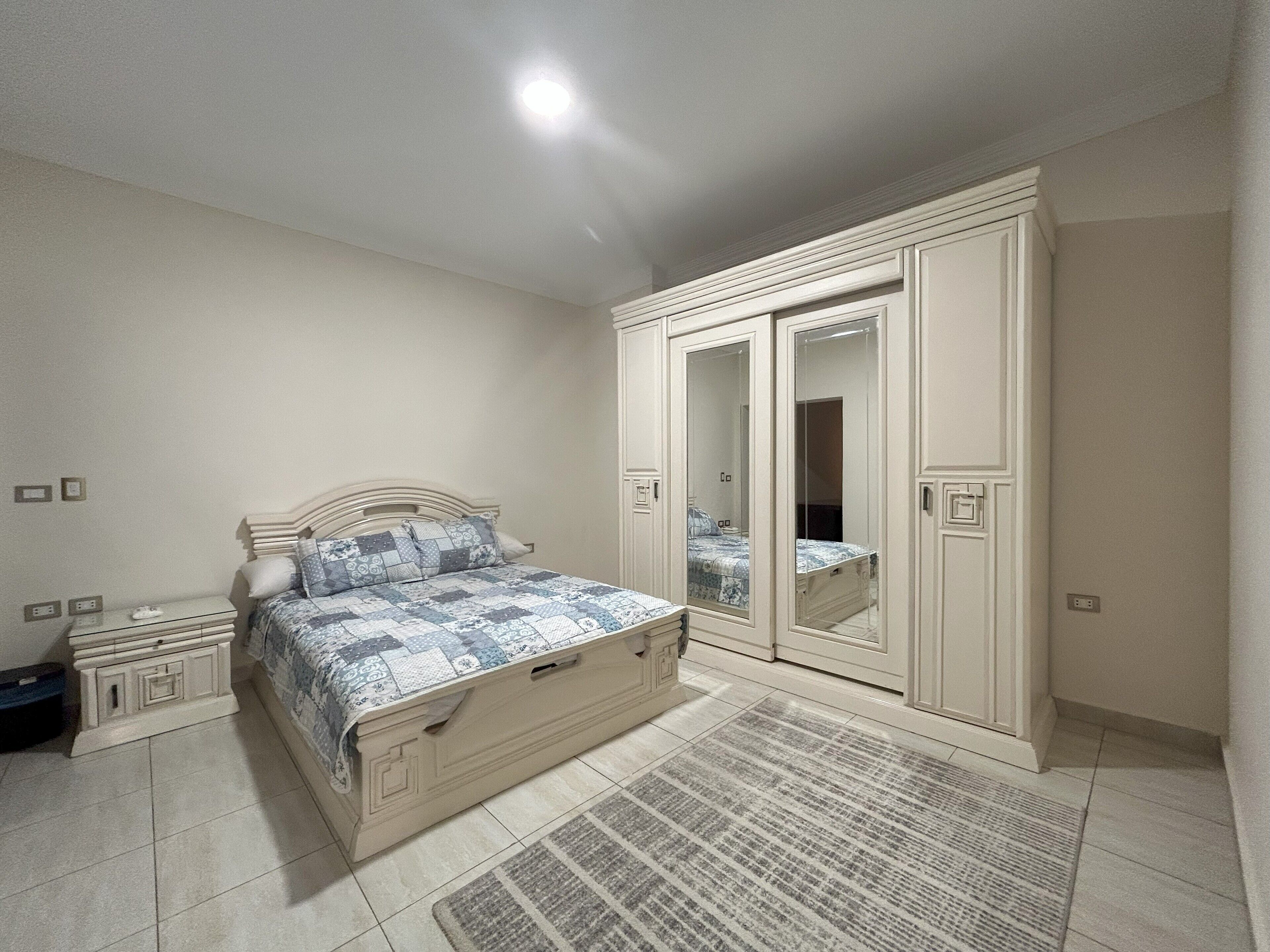 Een slaapkamer met een bed, een kledingkast, een spiegel en een nachtkastje.