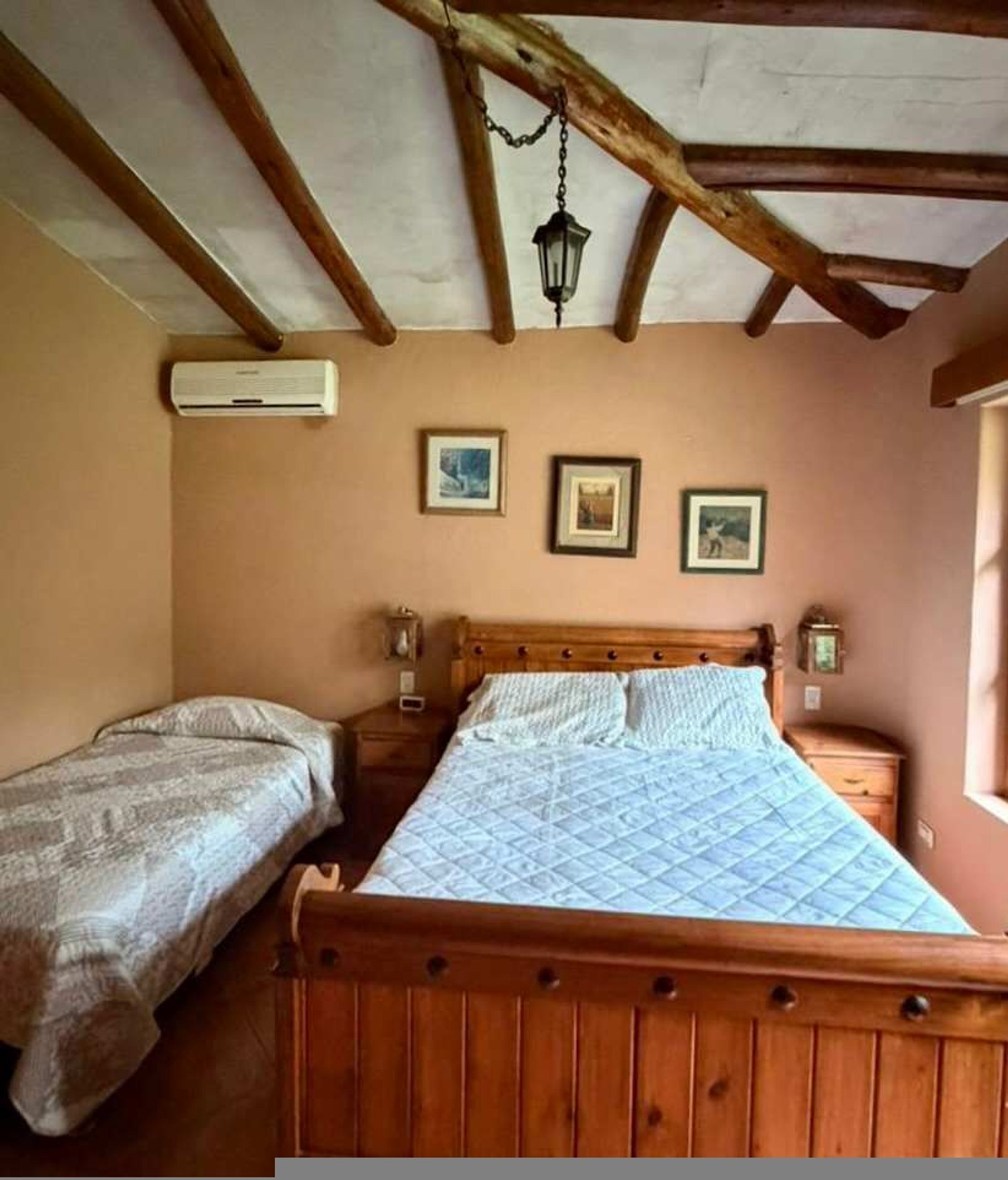 A bedroom with a wooden bed, two bedside tables, a hanging light fixture, and an air conditioning unit.
