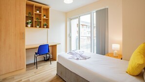 A hotel room with a bed, a desk, a chair, a wardrobe, a window, and a bedside lamp. - Modern 4BR Apartment in Central Limerick (Limerick)