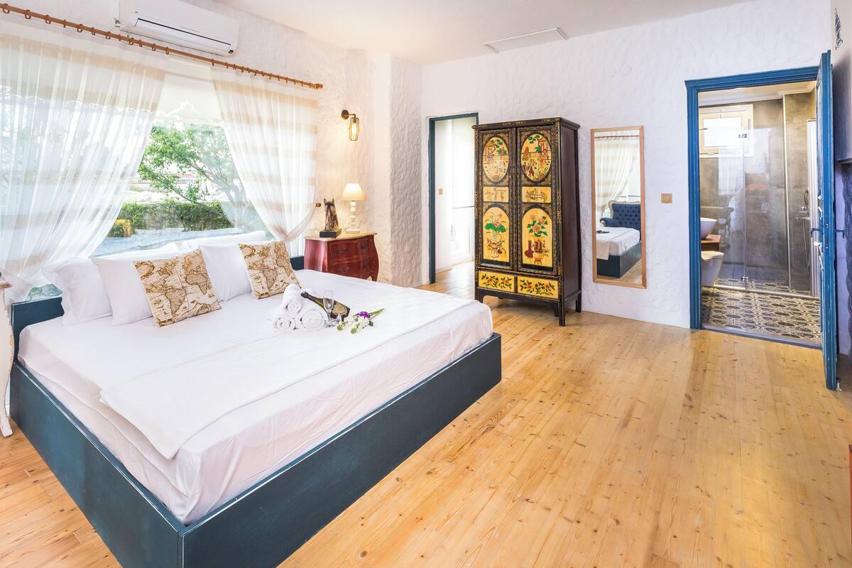 A bedroom with a large bed, a wardrobe, a mirror, and a shower area.