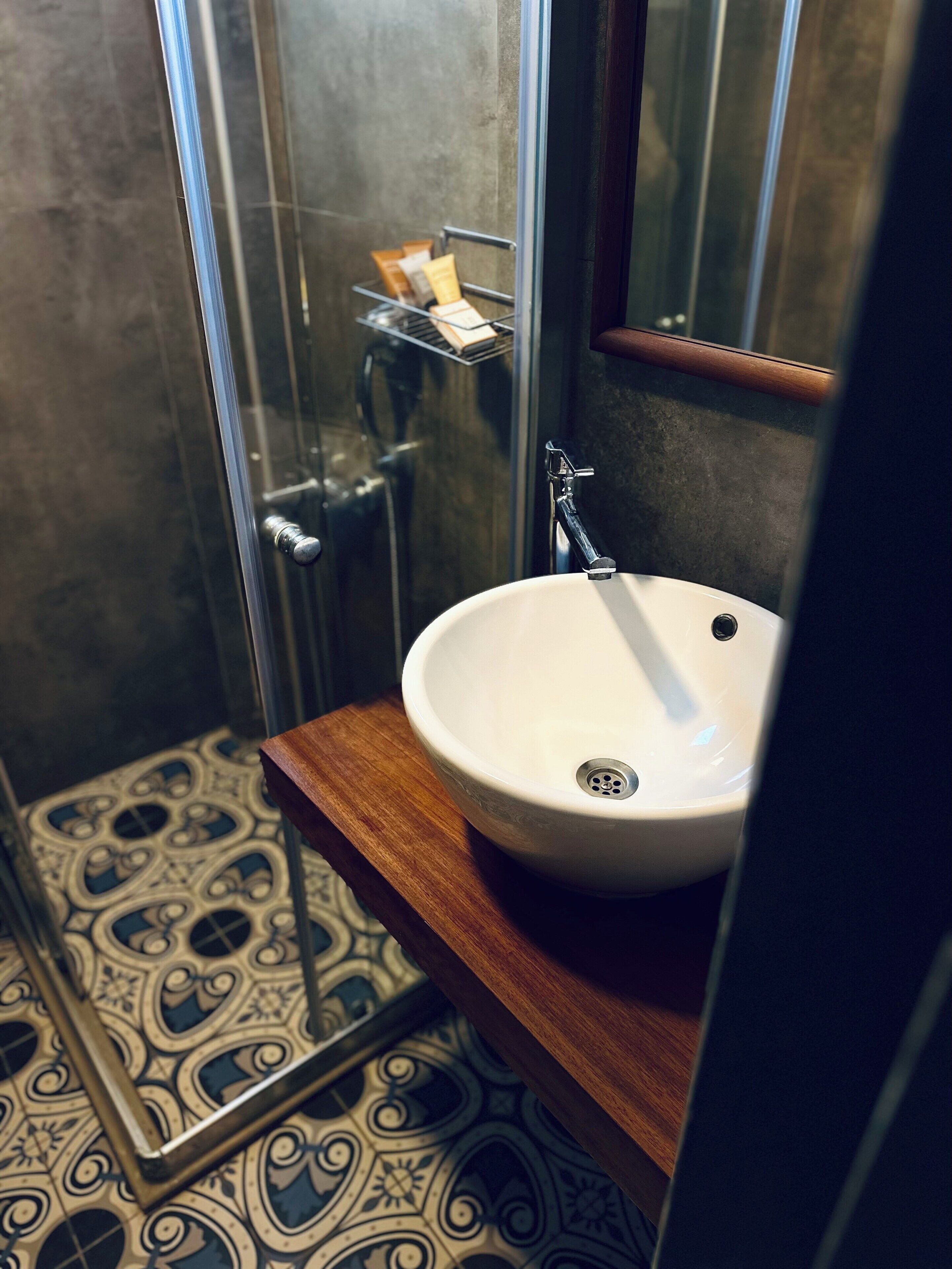 A bathroom with a white sink, a shower, and a patterned floor.