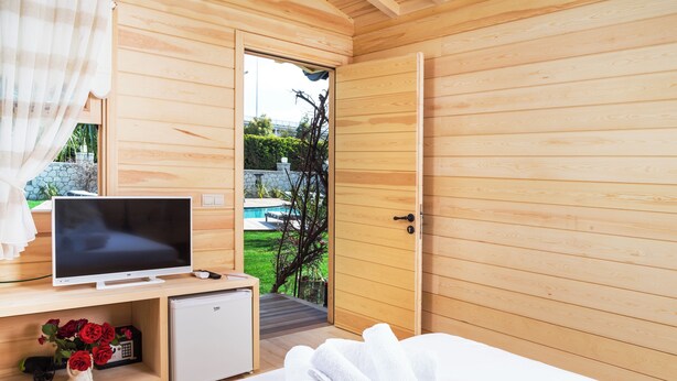 Una stanza in legno con un letto, una TV, un piccolo frigorifero e una porta che dà accesso a una zona piscina.