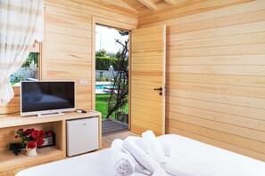 Ein Zimmer mit Holzboden, einem Bett, einem Fernseher, einer kleinen Kühlbox und einer Tür zum Poolbereich.