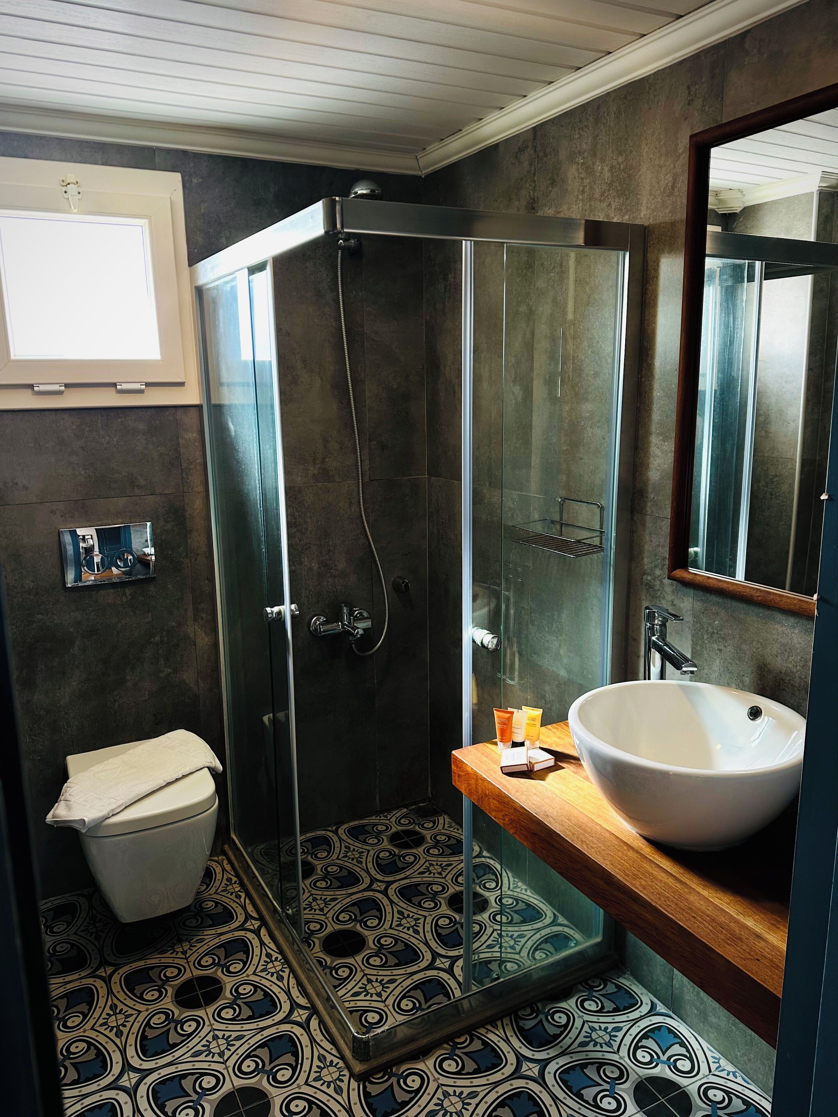 Un baño con ducha de vidrio, inodoro y lavamanos con espejo.