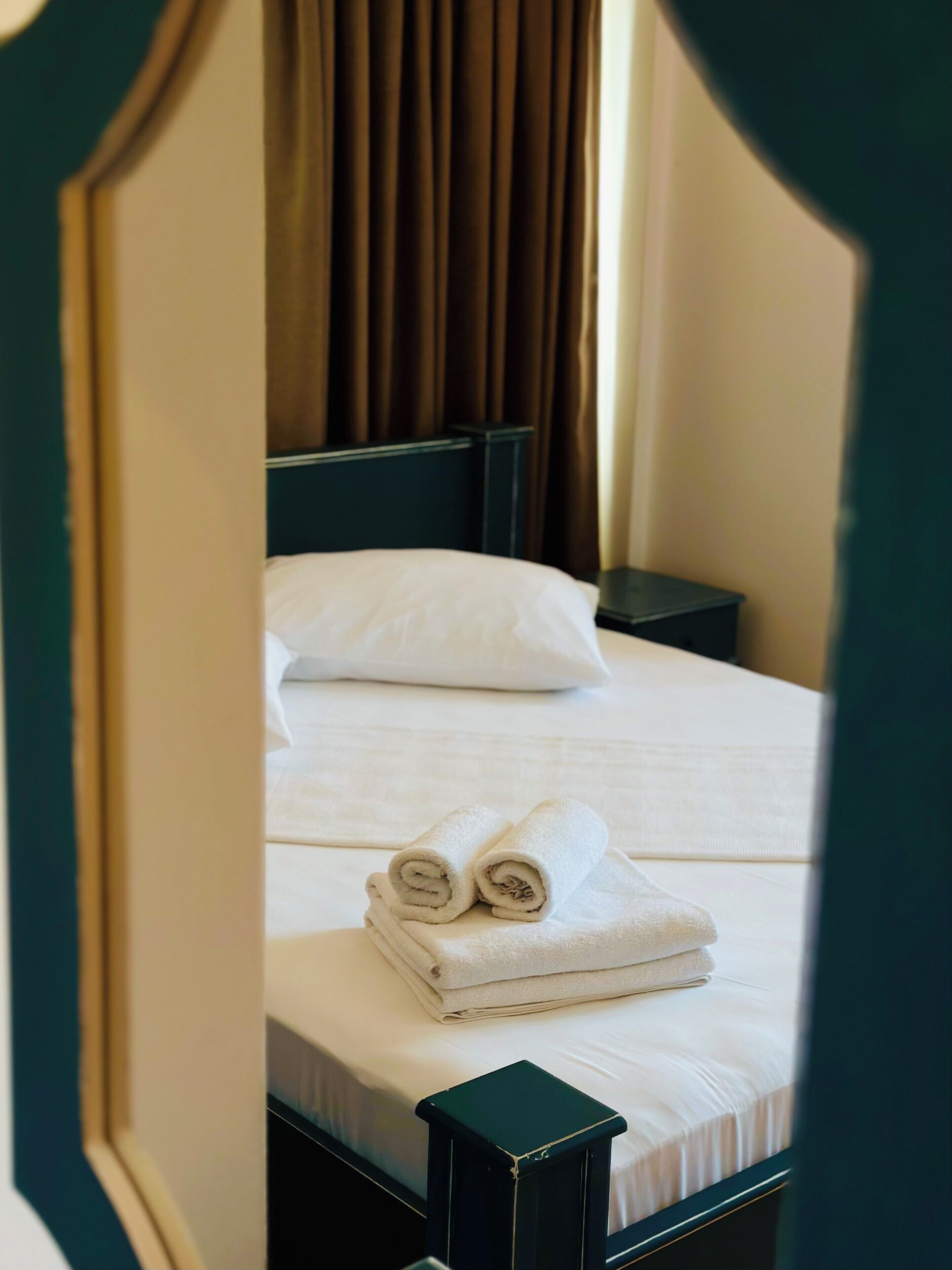 Un lit bien fait, avec du linge de lit blanc et des serviettes pliées, une tête de lit sombre et une petite table de chevet.