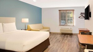 Une chambre d’hôtel équipée d’un lit, d’un bureau, d’une chaise, d’une lampe, d’une télévision et d’une fenêtre avec des stores.