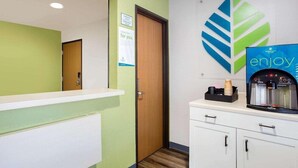 Un espace d’accueil d’hôtel avec un mur végétal, une porte en bois, un comptoir blanc et un distributeur d’eau.