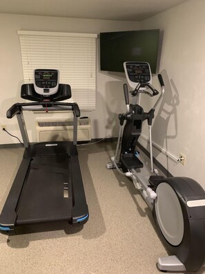 Un gimnasio en casa con una cinta de correr y una elíptica.
