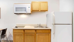 A compact kitchen with wooden cabinets, a white microwave, a sink, and a refrigerator. - Woodspring Suites Charlotte Shelby (Shelby)