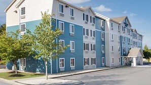 A multi-story hotel with a modern design, featuring a mix of white and blue exterior colors, a covered entrance, and a parking area. - Woodspring Suites Charlotte Shelby (Shelby)