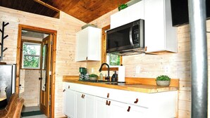 Un interior de madera con zona de cocina, que incluye armarios, un microondas y una cafetera.