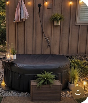 A hot tub with a wooden deck, a towel rack, potted plants, and candles. - Local Creek Tiny Home. Hot Tub. Wifi. Close to everything. Glamping. Private. (Knoxville)
