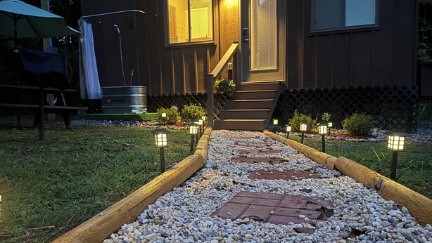 Una casa moderna con un camino de grava que lleva a la entrada, una cerca de madera e iluminación exterior.