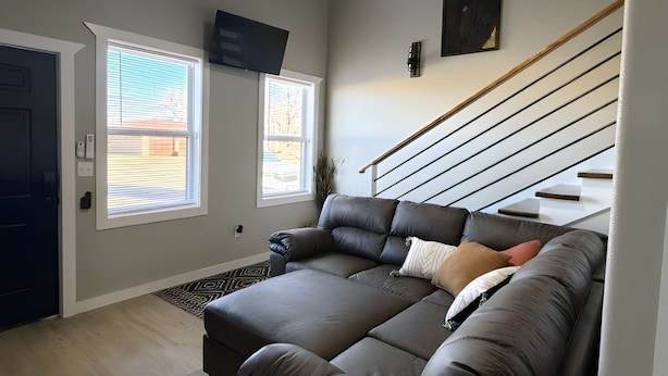 A living room with a sofa, a flat-screen TV mounted on the wall, a staircase, and a door.