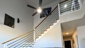 A modern living room with a sectional sofa, a staircase with a glass railing, and a ceiling fan.