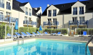 A swimming pool with lounge chairs and umbrellas, surrounded by apartment buildings with balconies. - Apartment in Audierne by Trescadec Beach (Audierne)