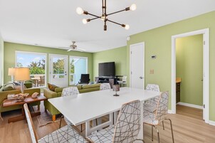 Una habitación con una mesa de comedor blanca, paredes verdes, un ventilador de techo y un televisor.