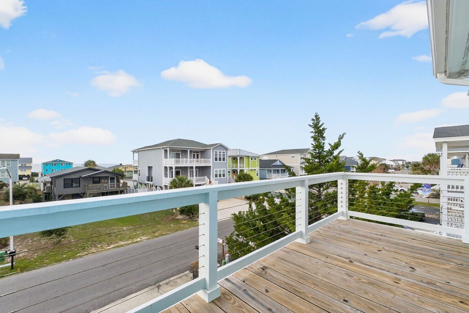 A wooden deck with a railing, overlooking a row of houses with a clear sky above.