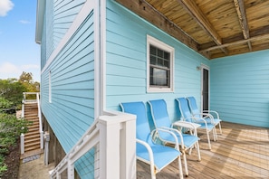 Ein blaues Haus mit Veranda, weißem Geländer und blauen Stühlen.