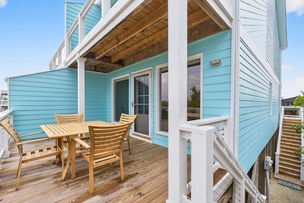 A covered deck with a wooden table and chairs, a white railing, and a blue exterior wall.