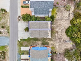 Vista aérea de una propiedad con un amplio espacio abierto, un edificio de techo gris y una sección cercada con vegetación.