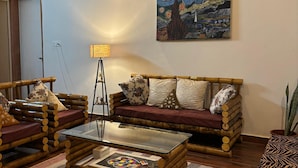 Un salon avec un canapé en bois, une table basse en verre, une lampe et un tableau accroché au mur.