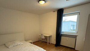 A bedroom with a bed, a desk, a chair, a window, and a radiator. - Beautiful 3 room apartment on the first floor with terrace and garden area (Deggendorf)