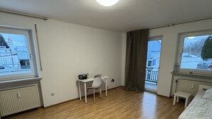 A room with a bed, a desk, and a chair. There are windows on two sides. - Beautiful 3 room apartment on the first floor with terrace and garden area (Deggendorf)