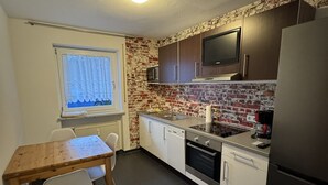 A compact kitchen with a dining table, chairs, a microwave, oven, and a refrigerator. - Beautiful 3 room apartment on the first floor with terrace and garden area (Deggendorf)