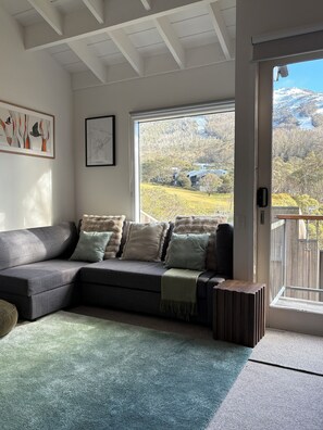 A modern living room with a sectional sofa, a framed map, and a view of a mountainous landscape through a large window.