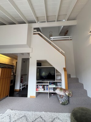 A modern living room with a staircase, a flat-screen TV, and a bookshelf.