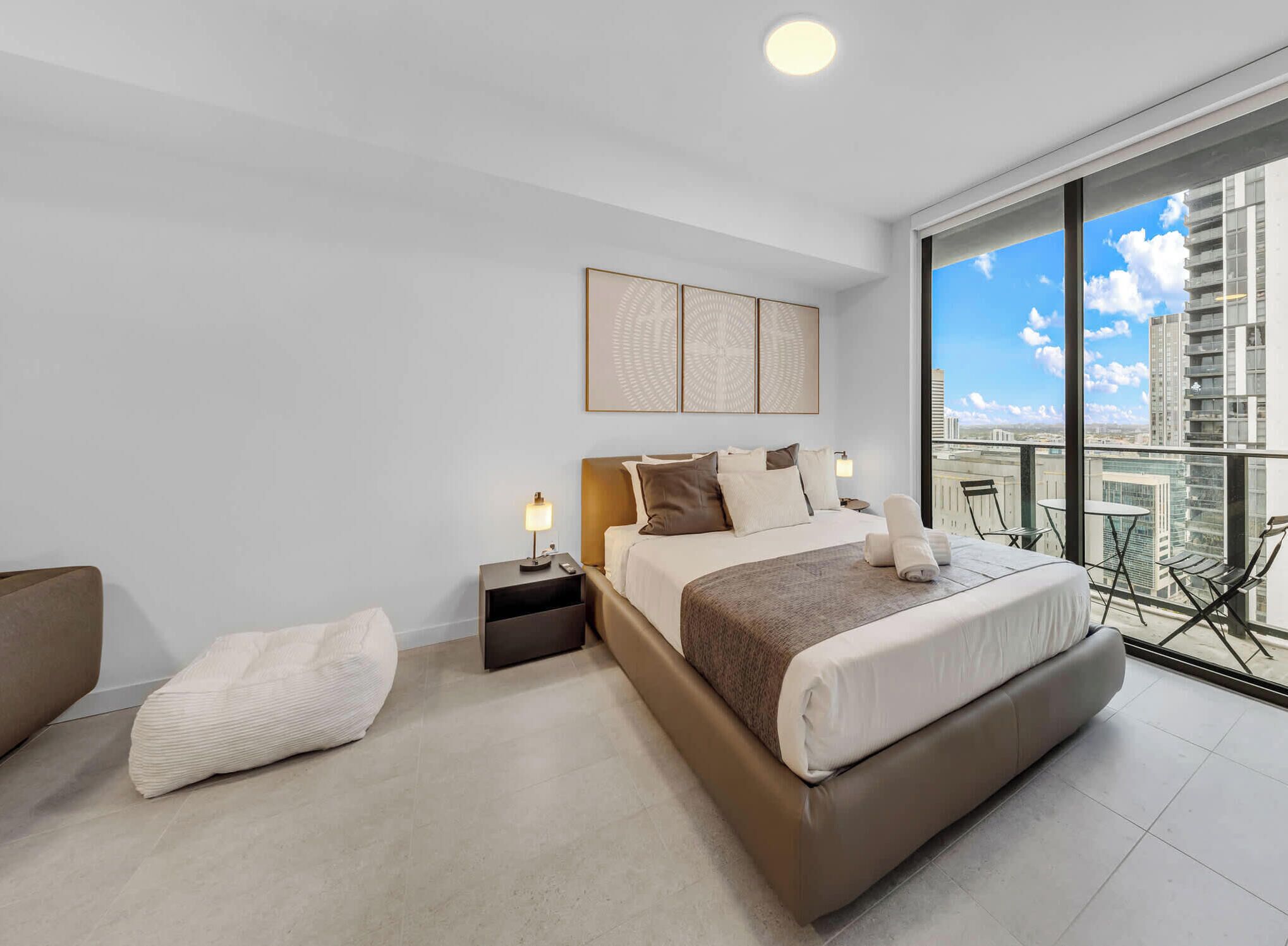 A modern hotel room with a large bed, a nightstand, a bedside table, and a balcony with a city view.