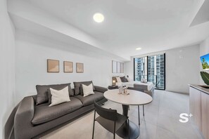 A modern living room with a grey sofa, a round dining table, and a large window with a city view. - Miami Condo | Rooftop Pool | 30th Floor Skyline Views (Miami)