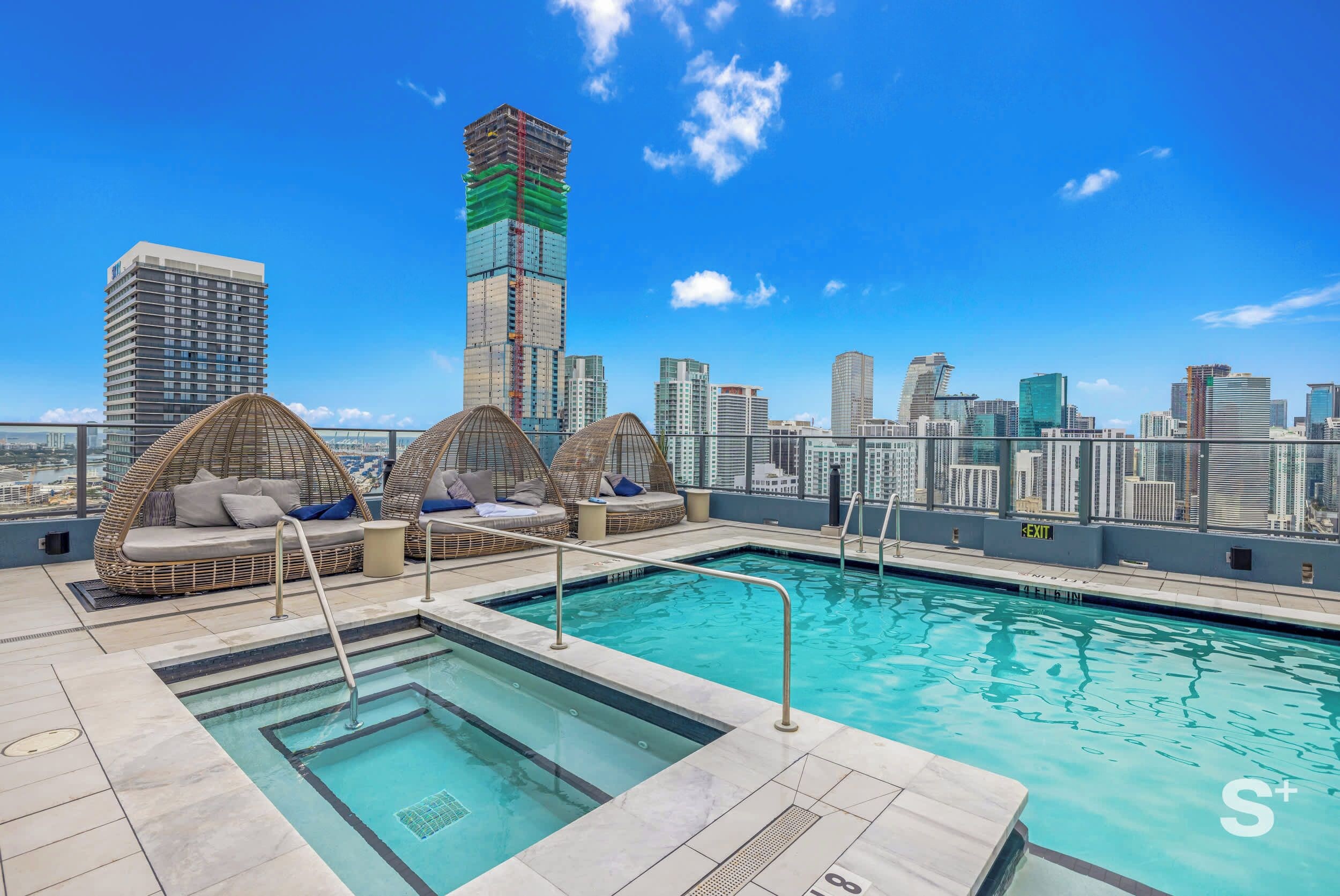 Stunning rooftop pool area featuring a sparkling pool, connected jacuzzi, and stylish shaded daybeds.
