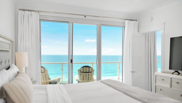 A hotel room with a large bed, a TV, a chair, and a view of the ocean. - Incredible condo, Newly Renovated Gulf-Front Luxury with Stunning Views. (Destin)