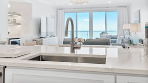 A modern kitchen with a stainless steel sink, white cabinetry, and a view of the sea through large windows. - Incredible condo, Newly Renovated Gulf-Front Luxury with Stunning Views. (Destin)