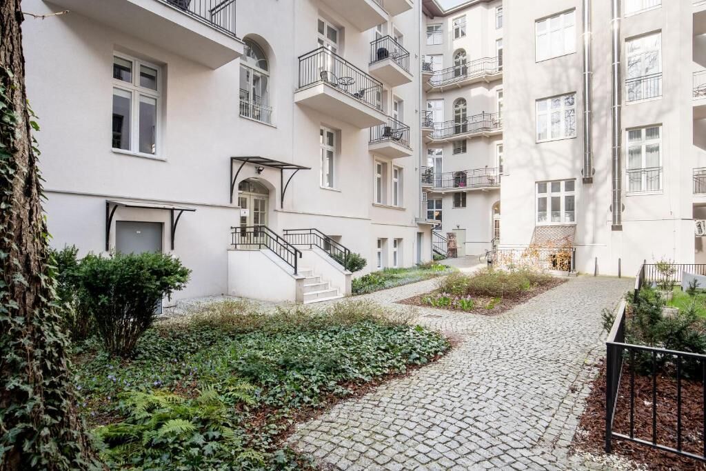 Um edifício residencial com vários andares, varandas, um caminho de pedras e uma pequena área de jardim.