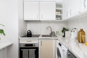A compact kitchen with white cabinets, a built-in oven, a washing machine, and a sink. - Malila Apartments Starowiślna 35 (Kraków)