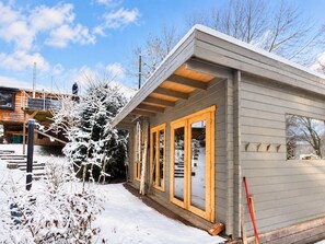 Ein modernes Blockhaus mit einer Holzterrasse, großen Fenstern und verschneiter Landschaft.