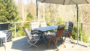 Une terrasse extérieure avec une table et des chaises, un grand parasol et une vue sur les arbres.