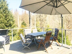 An outdoor deck with a table and chairs, a large umbrella, and a view of trees. - Ferienhaus Allrode mit Wellness (Thale)
