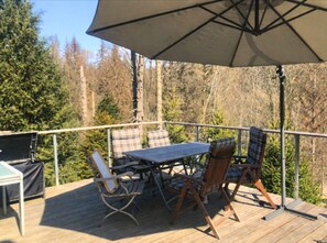 A deck with a table and chairs, surrounded by a railing, overlooking a forested area. - Ferienhaus Allrode mit Wellness (Thale)